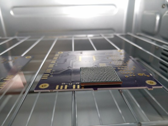 Upside down BGA sitting on a scrap PCB in the oven