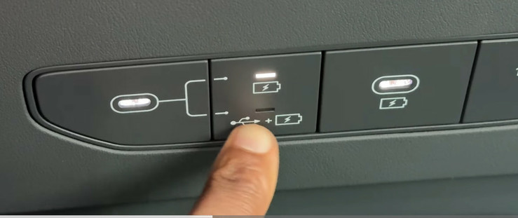 A photo of a YouTuber’s finger pointing at a button on the new Kia EV9 that shows two modes next to a USB port.  The symbols indicate two choices:  Battery only, or battery with USB data.