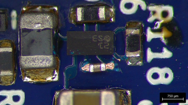 Closeup of a tiny 0201 capacitor straddling the vias after removal of soldermask