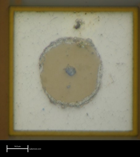 Microscope photo showing a white square structure surrounded by a thin gold colored outline, with a tannish circle in the middle and some roughness at the boundary