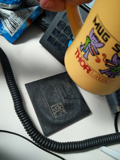 Thorlabs mug being picked up to show a custom slate coaster laser engraved to look like an Artix-7 FPGA