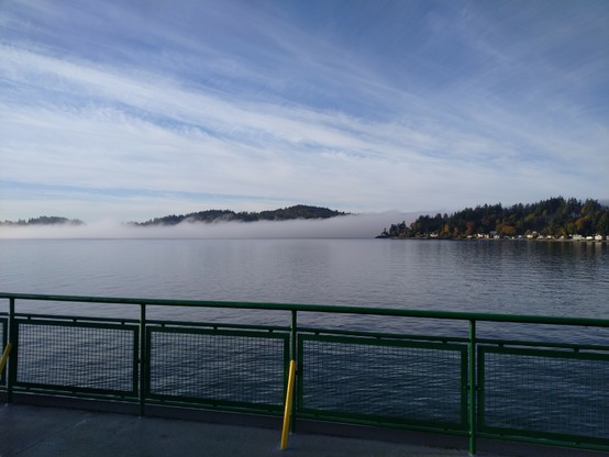Looking to the left, another low lying fog bank covers the water but taller hills on the shore, lined with tall pine trees, are poking out of the top of the fog showing it's very low to the water