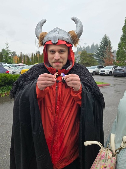 Me, white male with a mustache and some stubble, wearing a horned "Viking helmet" and a black faux-fur cloak while holding two tiny toy unicorns.

A red raincoat is poking out from under the costume because it's raining.