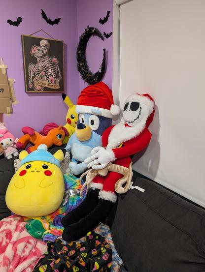 A large pile of Christmas themed plushies on a couch including Bluey in a santa hat, Pikachu in a winter hat, and Jack Skellington