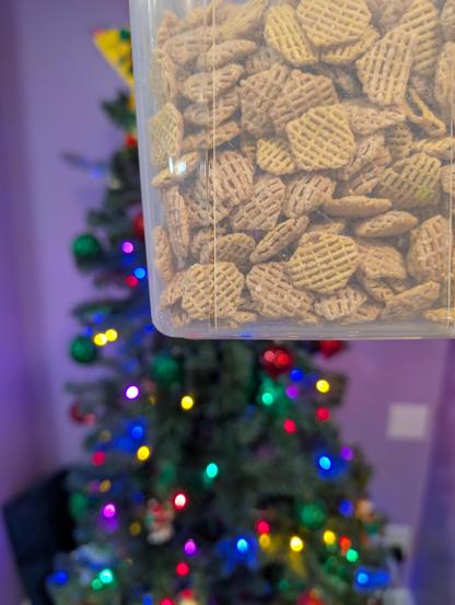A plastic storage box full of Crispix cereal held in front of a Christmas tree
