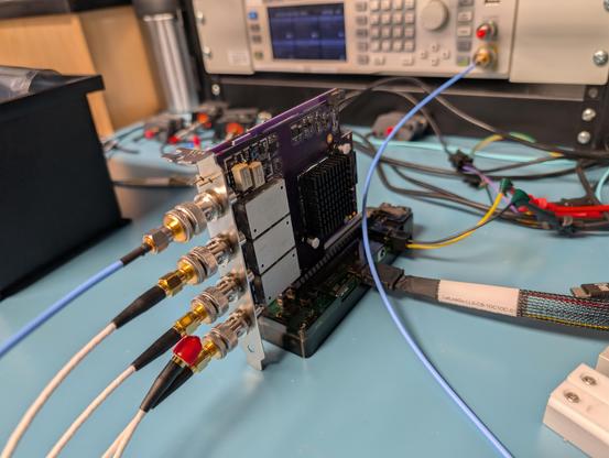 Purple PCIe oscilloscope card with blue and white coaxial cables coming off the four BNC ports, plugged into a desktop PCIe riser card